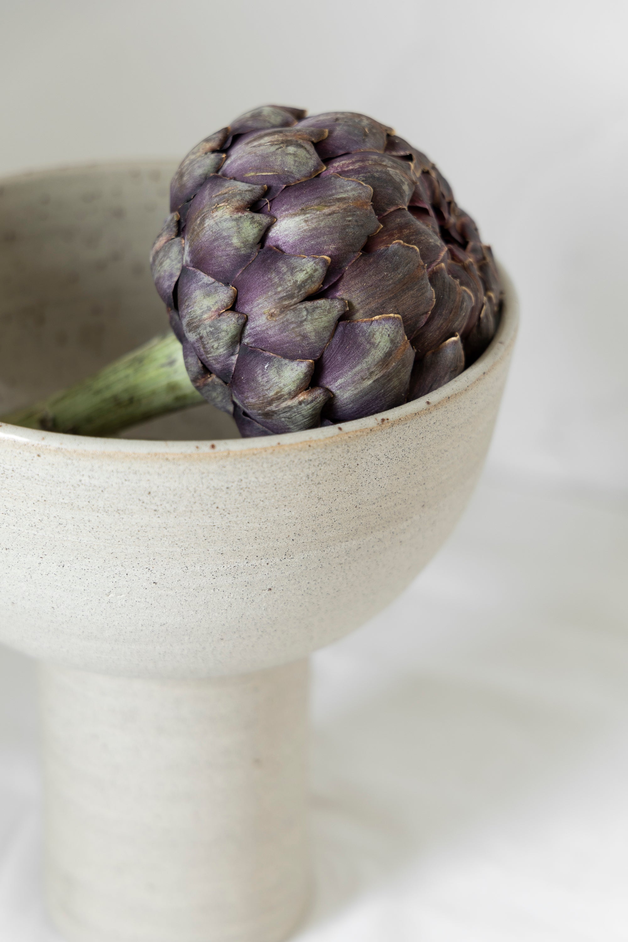 Paarse artisjok in een handgemaakte keramische kom met minimalistisch design.